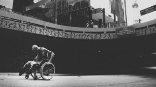 コンクリートの坂道を車椅子で進む男性のモノクロ写真